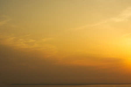 A wonderful nature cover with different shades of yellow-brown sky, some clouds, and a hint of a Sun itselfの写真素材