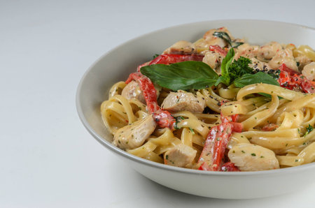 Bowl of pasta with chicken and capcicum served with leaves of fresh basil on white backgroundの写真素材