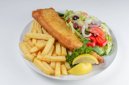 Traditional fish and chips served with lemon and salad on white plateの写真素材