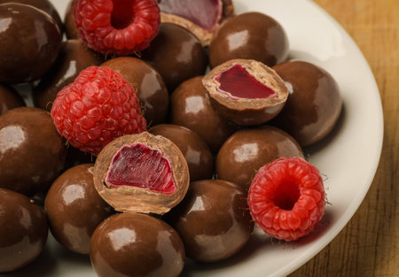 Milk chocolate coated jelly candies and fresh raspberry on white plateの写真素材