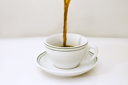 Black coffee being poured on a white cup over white backgroundの写真素材