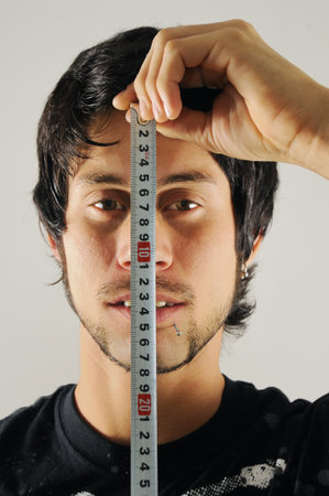 Portrait of a young man with measure tape measuring his faceの写真素材