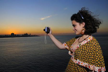Portrait of young woman taking picture with compact camera outdoors at sunset