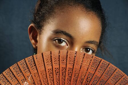Portrait of african teen girl covering her face with fanの写真素材