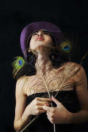 Portrait of young trendy girl holding peacock feathers under disco lights backgroundの写真素材