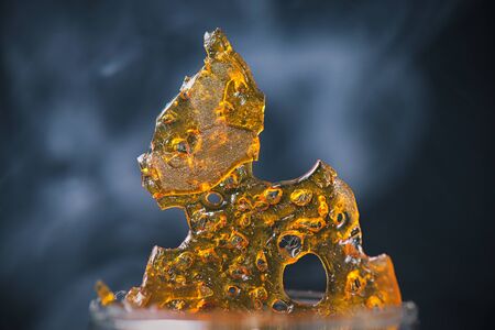 Abstract detail of cannabis oil concentrate aka shatter with smoke over dark backgroundの写真素材