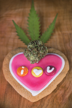 Dried cannabis nug with with pot leaf over baked cookies on a wood tray - infused marijuana edibles conceptの写真素材