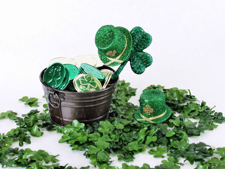 A metal bucket with coins on a bed of clover, green leprechaun hats all around, on a white backgroundの写真素材