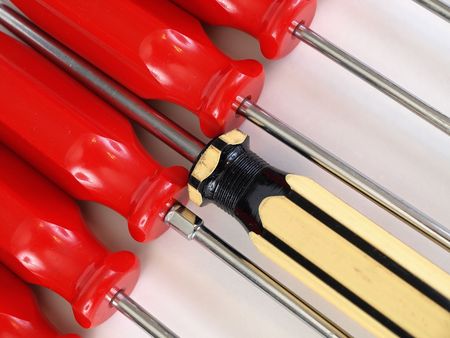 Red handled screwdrivers with a yellow and black handled one pushing in. Over white.の写真素材