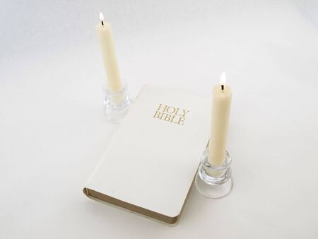 A white Holy Bible between two white lit candlesticks on a white background.の写真素材