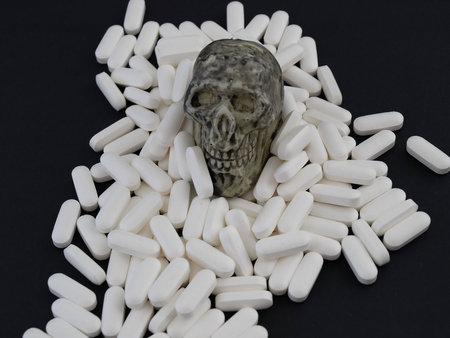 A small skull sits on a heap of white pills.  Studio isolated on a black .の写真素材