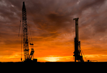 Crane and a drill standing tall at sunset.の写真素材