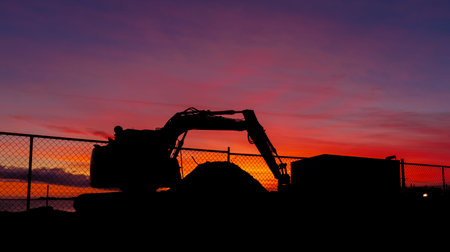 Excavator parkup for a the end of the day. with a woinderful hot red sunset sky behind it.の写真素材