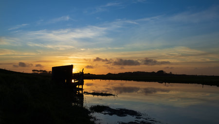 Sunset behind a pond shed with a wonderful water reflection.の写真素材