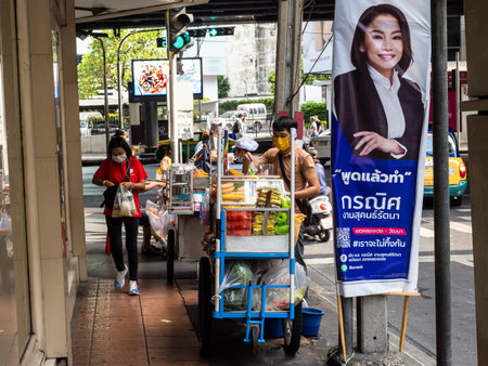In the midst of a global pandemic, a street vendor and customer exchange goods with masked faces outside the bustling Phrom Pong Skytrain station in Bangkok, Thailand. The image captures the resilience and adaptability of the city's inhabitants in the facのeditorial素材