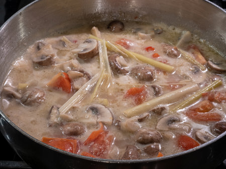 Vegetarian-style Tom Kha Thai soup simmering in a pot, featuring creamy coconut milk, savory mushrooms, tangy tomatoes, and aromatic lemongrass.の写真素材