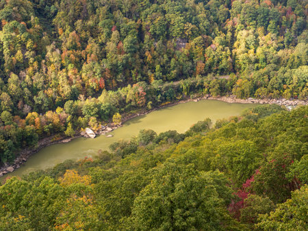Sunlight highlights the fall-colored mountainside above the water at New River Gorge National Park, West Virginia, creating a stunning autumn landscape.の写真素材