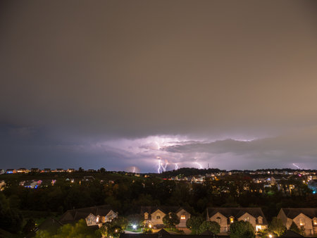 Dark storm clouds loom over an American neighborhood, with brilliant lightning illuminating the sky in a thrilling display of nature's power.の写真素材