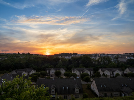 A picturesque view of a suburban community bathed in the warm hues of a setting sun, with fluffy clouds adding a touch of drama to the sky.の写真素材