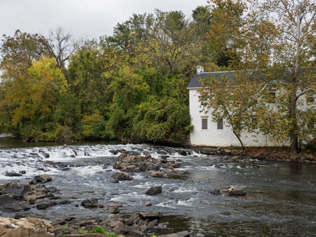 A wide view of a white historic mill building next to the creek, featuring rushing rapids and rocks in the foreground.の写真素材