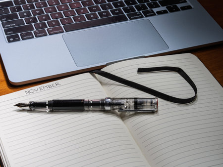 An open notebook shows November handwritten on the page next to a clear fountain pen and laptop on a...