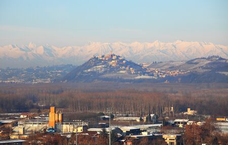 View on industrial zone and small town on snowy hill in front of snowy mountains in Piedmont, northern Italy.の写真素材