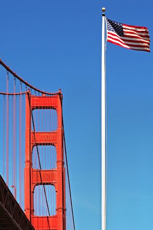 Vertical oriented image of Golden Gate Bridge and American National Flag waving on the wind in San Francisco, USA.の写真素材