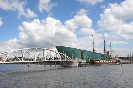 Modern bridge over Amstel river and vintage ship standing nearfamous Nemo Building in Amsterdam, Netherlands.の写真素材