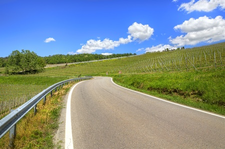 Curved road passes through green hills and vineyards under beautiful blue sky with white clouds in spring in Piedmont, northern Italy.の写真素材