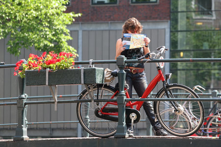 AMSTERDAM - JULY 16: Unidentified woman holds Amsterdam city map and stands near red bicycle on the bridge.Bicycles are the most used mode of transport and very popular with tourists and locals in Amsterdam, Netherlands on July 16, 2007.のeditorial素材