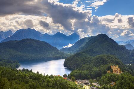 Aerial view on medieval castle on the hill near alpine lake among mountains under cloudy sky in Bavaria, Germany の写真素材