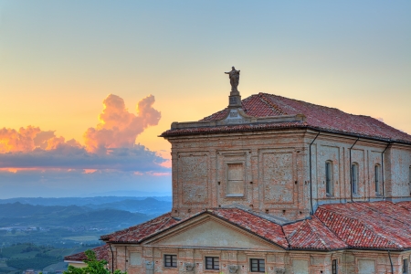 Statue of Jesus Christ on the church roof and hills of Langhe on background at sunset under beautiful evening sky in Piedmont, Northern Italy の写真素材