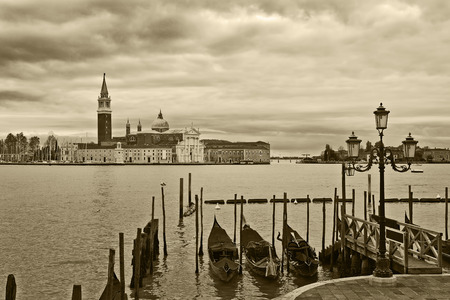 Tied gondolas on Grand Canal and San Giorgio Maggiore church on under cloudy sky in Venice, Italy  sepia toned  の写真素材