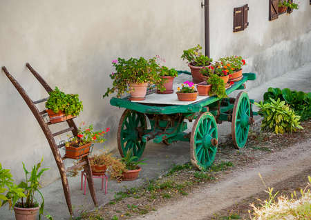 Pots with flowers on top of green wooden cart as part of rural garden decoration in Piedmont, Italy の写真素材