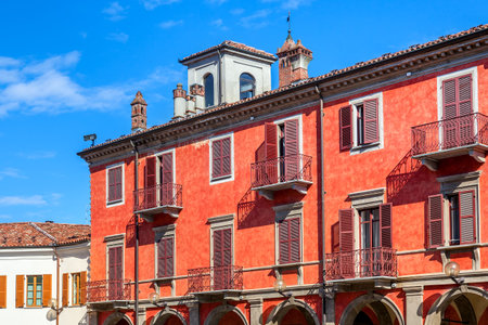 Facade of red two storey building with balconies and wooden shutters under blue sky in Alba, Italy の写真素材
