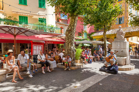 MENTON, FRANCE - AUGUST15, 2014: People listening to street musician on small square in old town of Menton - popular tourist resort on French Riviera, famous for its gardens and annual Lemon Festival taking place every February.のeditorial素材