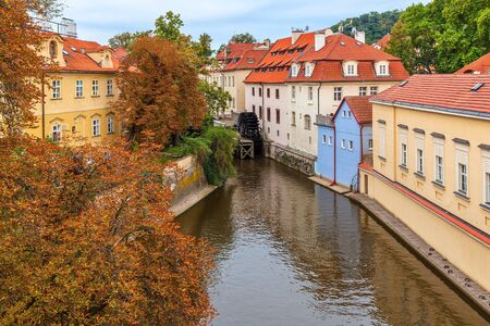 Narrow canal among colorful houses with red roofs and autumnal trees in Prague, Czech Republic.の写真素材
