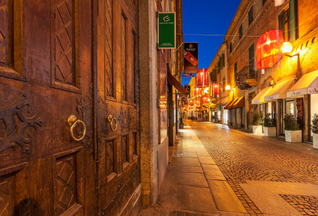 ALBA, ITALY - DECEMBER 30, 2014: Old wooden door and pedestrian street with shops in old town illuminated for Christmas and New Years celebrations. This area is very popular with locals and tourists visiting Alba for winter holidays.のeditorial素材