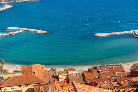Red roofs overlooking shoreline and blue water of Mediterranean sea in Menton, France.の写真素材
