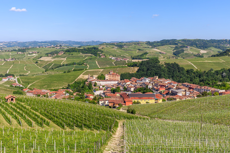 Small town of Barolo among hills with green vineyards under blue sky in Piedmont, Northern Italy.の写真素材