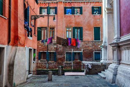Small square surrounded by typical colorful houses with laundry on windows in Venice, Italy.の写真素材