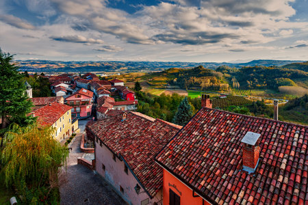 View of houses with tile roofs and autumnal hills of Roero on background in small town of Monticello...