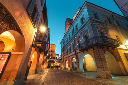 Cobblestone pedestrian street illuminated in evening in Old Town of Alba, Piedmont, Northern Italy...