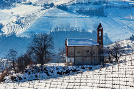 Small parish church among vineyards on snowy hills in Piedmont, Northern Italy.の写真素材