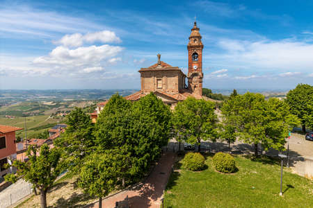 View of old catholic church among green trees under beautiful blue sky with white clouds in small town of Diano d'Alba, Piedmont, Northern Italy.の写真素材