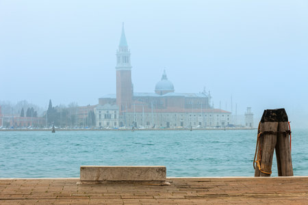 Lone stone bench and view of San Giorgio Maggiore church in the fog in Venice, Italy.の写真素材