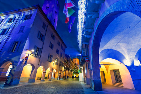 Low angle view of the evening narrow cobble street among historic buildings illuminated with Christmas lights in Alba, Italy.の写真素材
