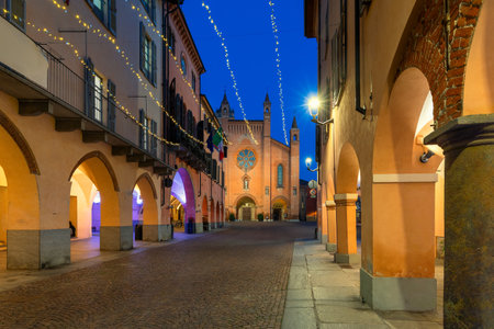 View of the narrow cobblestone street among historic buildings illuminated with christmas lights as San Lorenzo cathedral on background in Alba, Italy.の写真素材