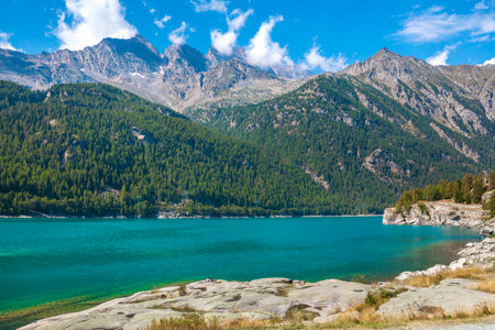 View of the alpine lake of Ceresole Reale and mountains under beautiful blue sky with white clouds in Piedmont, Italy.の写真素材