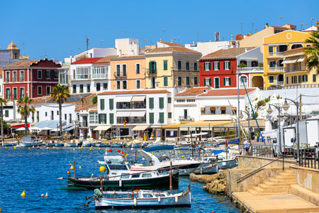 A picturesque Mediterranean harbor with boats moored in the calm water on a sunny day as colorful houses on background in Mahon, Balearic Islands, Spain.の写真素材
